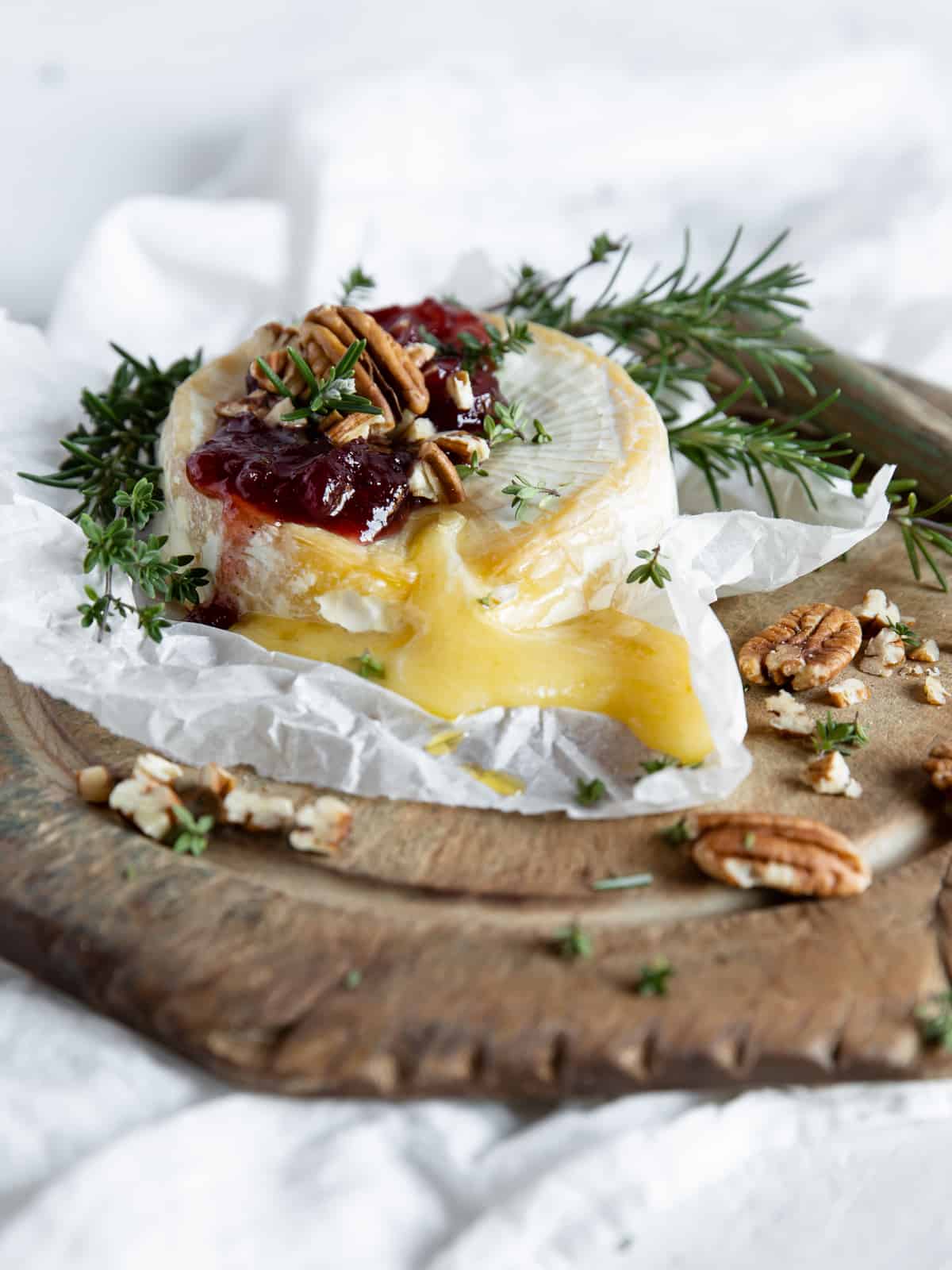 baked brie with cranberry sauce and pecans, garnished with fresh herbs and served with crackers