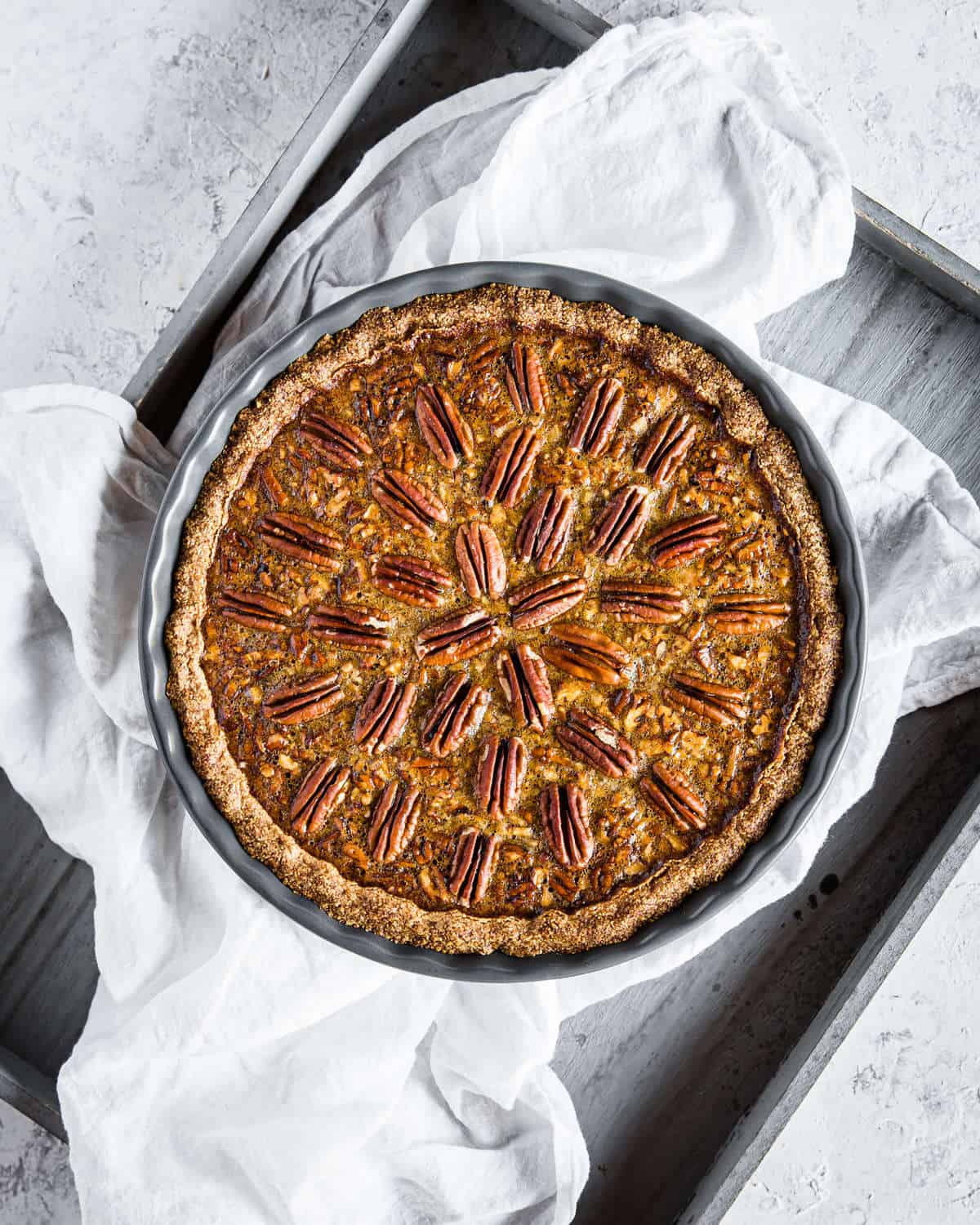 overhead shot of a low carb and gluten free pecan pie, in a pie tin, served on a wooden serving tray with a white linen.