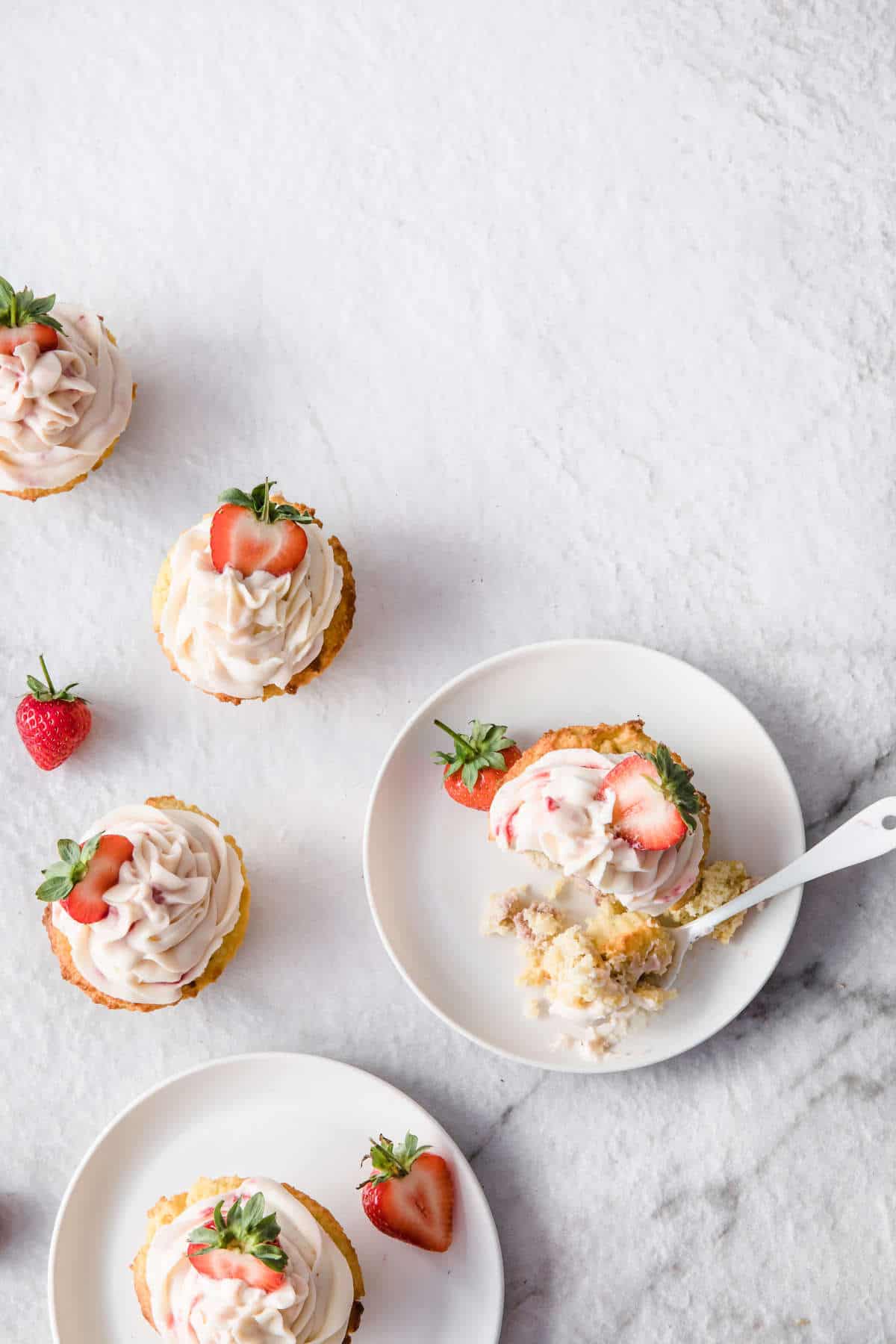 low carb strawberry lemonade cupcake with strawberry frosting on a white plate with a bite taken out of it