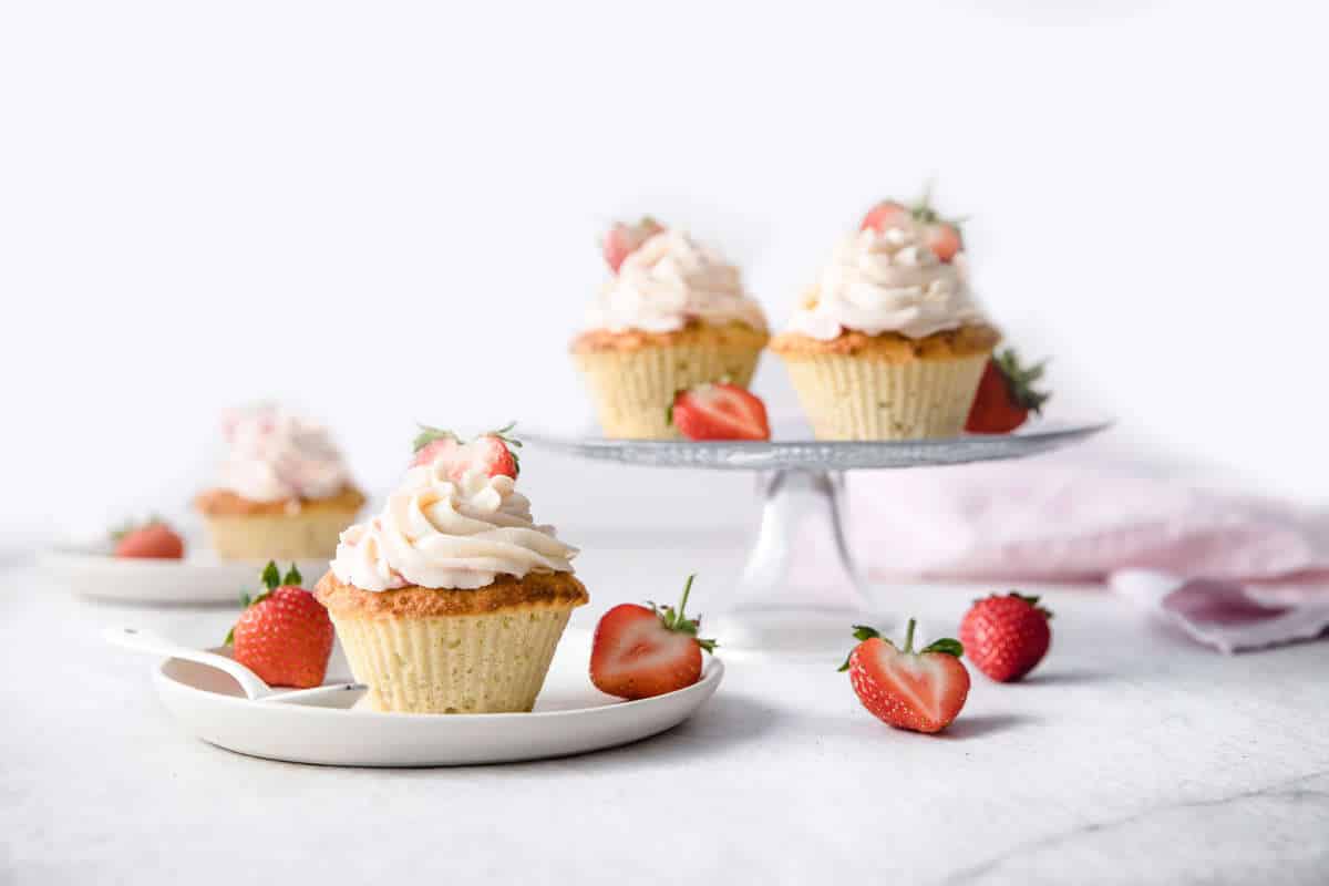 lemon cupcakes frosted with strawberry cream cheese frosting, served on a cake stand, with fresh strawberries