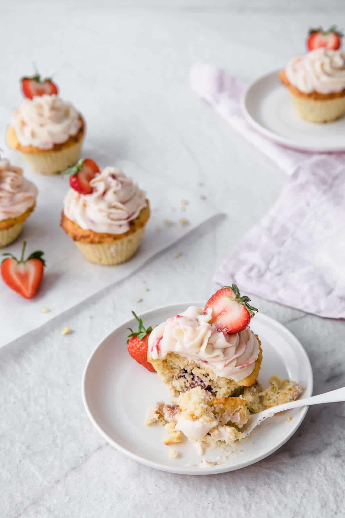 low carb strawberry lemonade cupcake with strawberry frosting on a white plate with a bite taken out of it