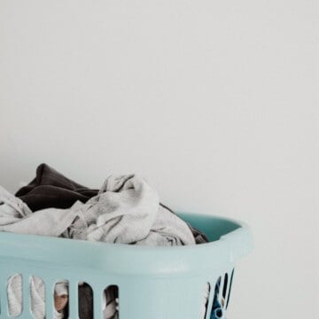A pile of laundry in a light teal laundry basket sits against a white wall.