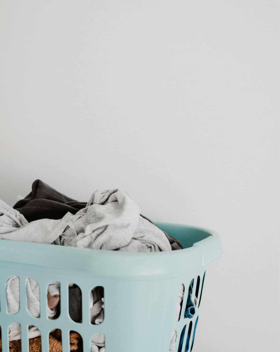 A pile of laundry in a light teal laundry basket sits against a white wall.