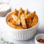 white bowl filled with crispy potato wedges, garnished with fresh thyme