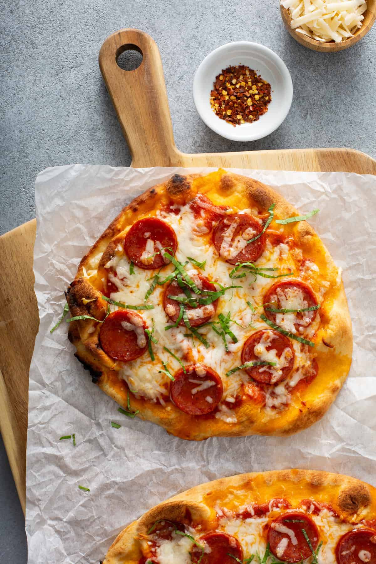 a wooden pizza paddle topped with pepperoni pizza, garnished with fresh basil and red pepper flakes