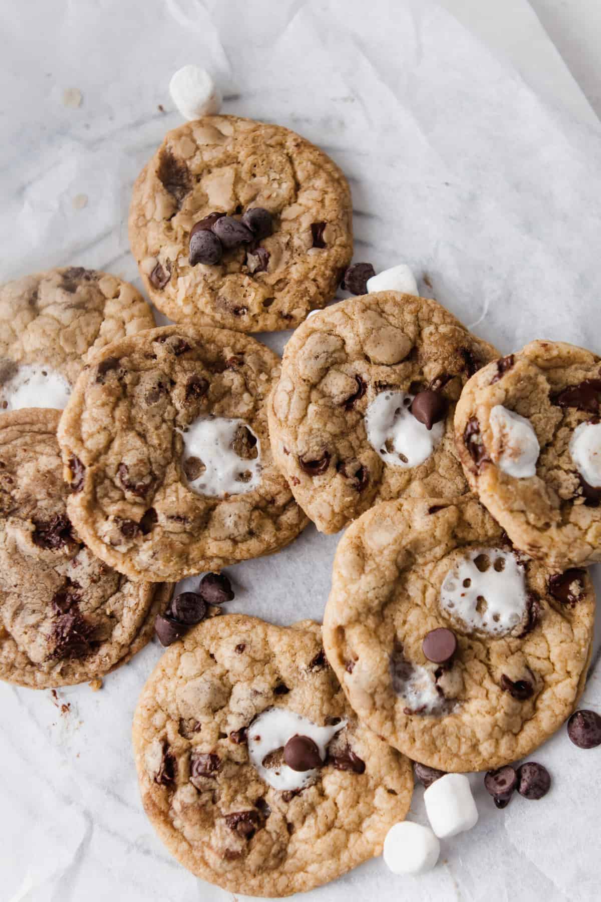 a pile of chocolate chip cookies with mini marshmallows and chocolate chips around it