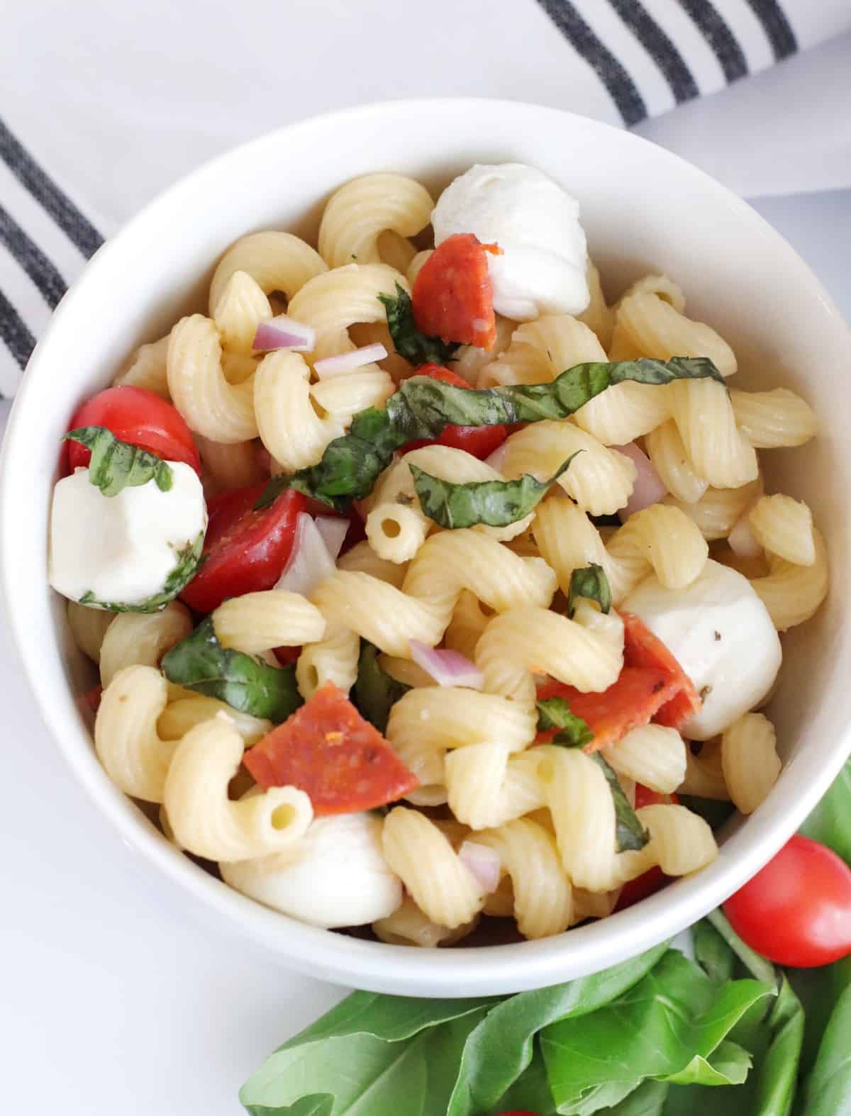 white bowl with pasta salad made of cavatappi, pepperoni, basil, tomatoes, and fresh mozzarella