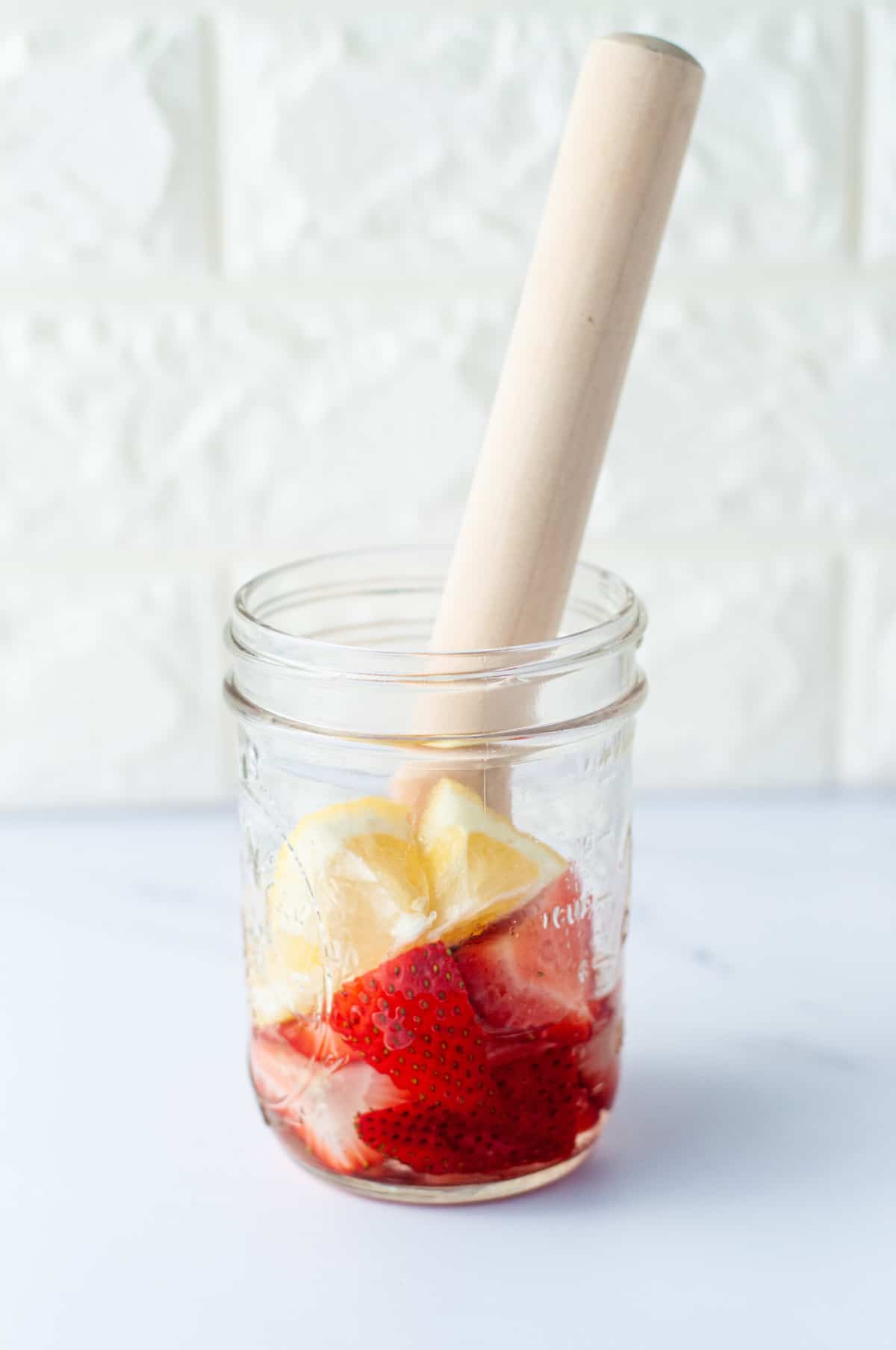 a mason jar with vodka, strawberries, lemons and a muddler