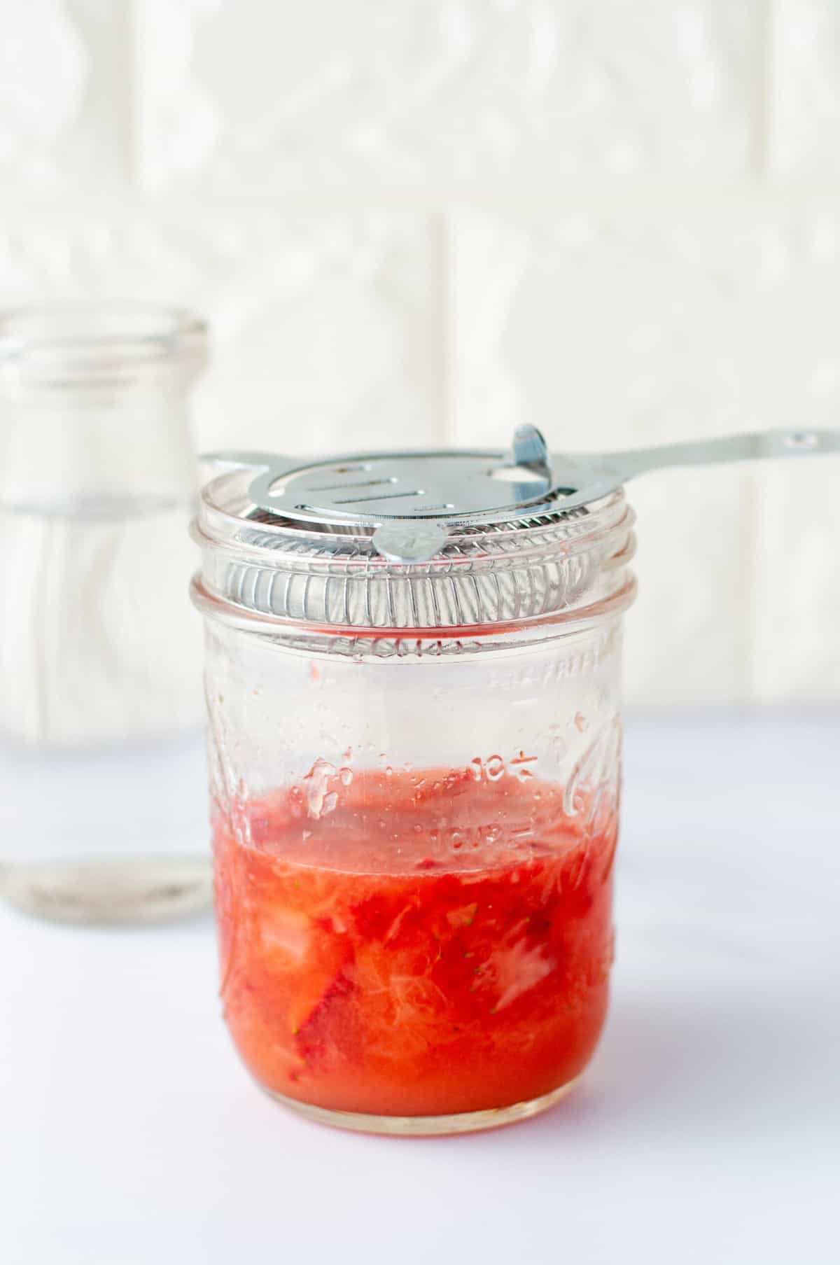 a mason jar with vodka, strawberries, lemons all muddled together with a strainer lid