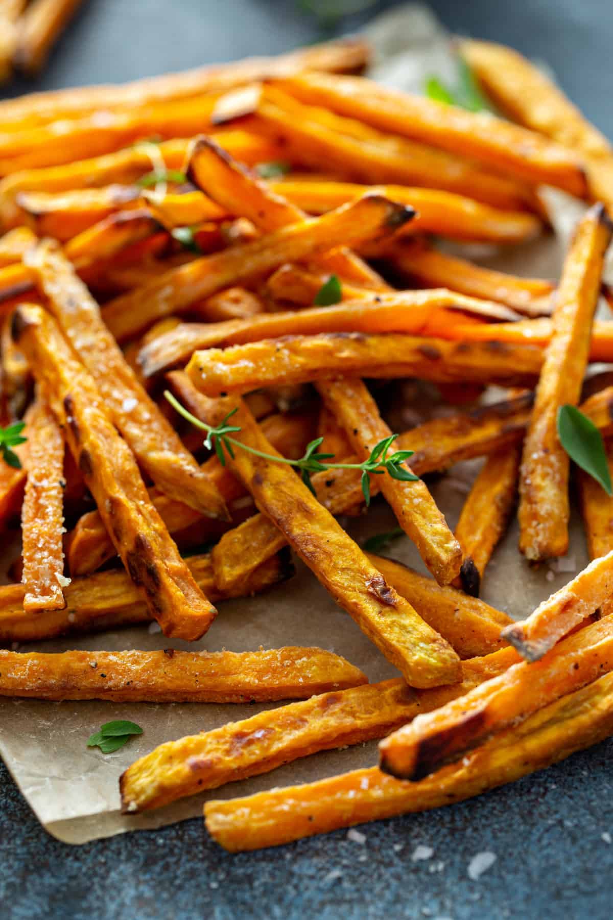 A serving dish lined with parchment paper, topped with crispy air fryer sweet potato fries, sea salt and fresh herbs.