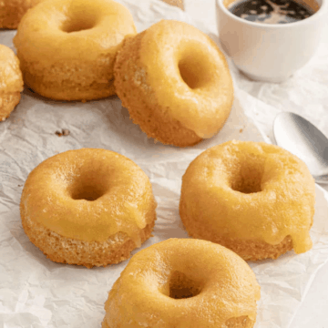 low carb glazed donuts piled up on white parchment paper served with a mug of black coffee.