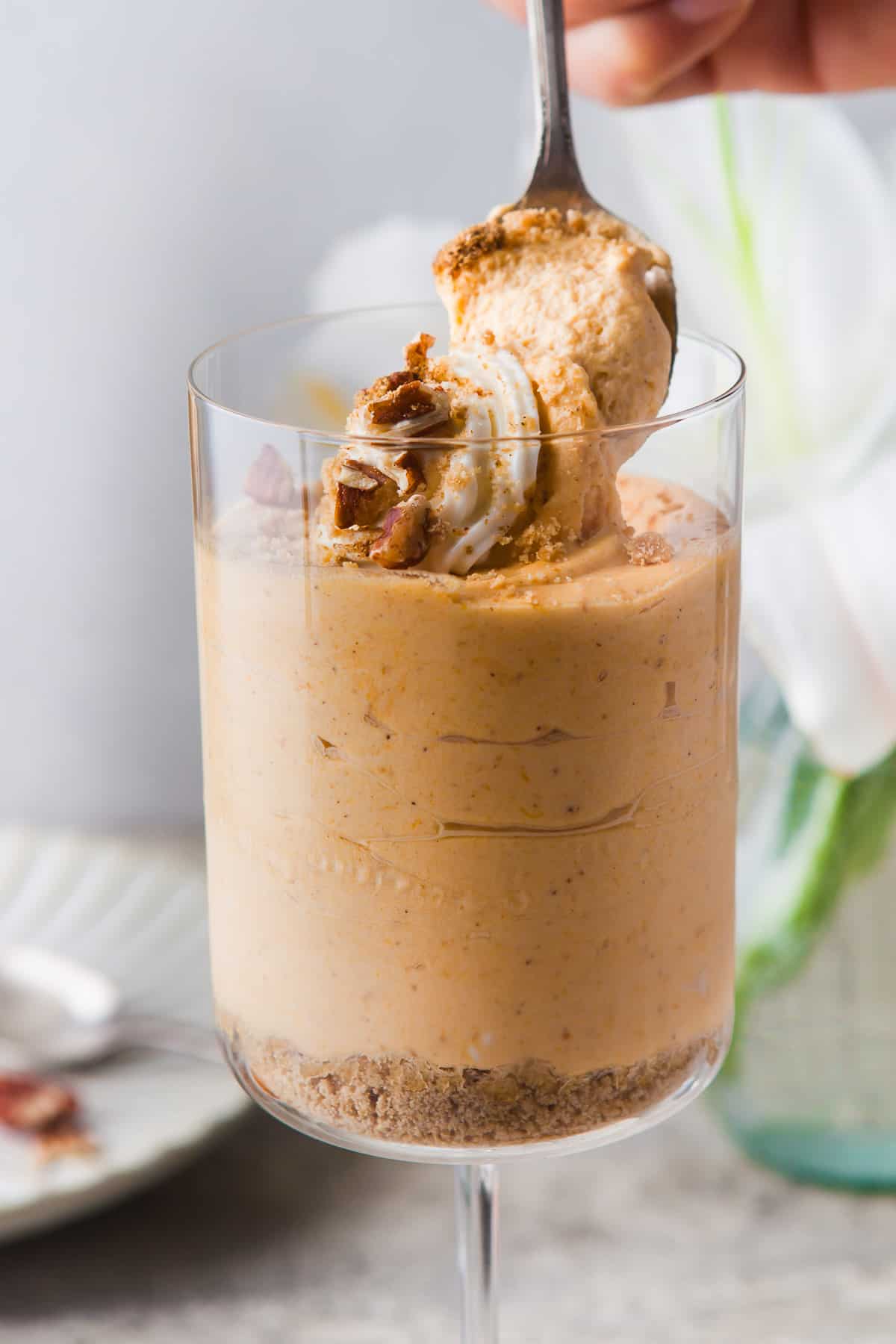 a large wine glass, filled with a pumpkin mousse, topped with shipped cream, nuts and spices
