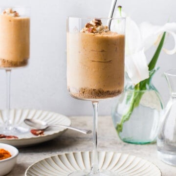 a large wine glass, filled with a pumpkin mousse, topped with shipped cream, nuts and spices