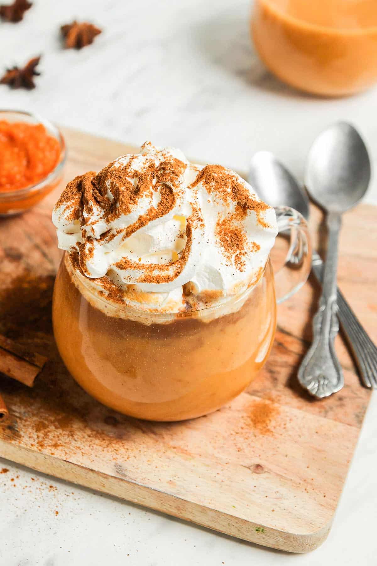 a clear glass mug with a pumpkin spice latte, topped with whipped cream and a sprinkle of pumpkin pie spice