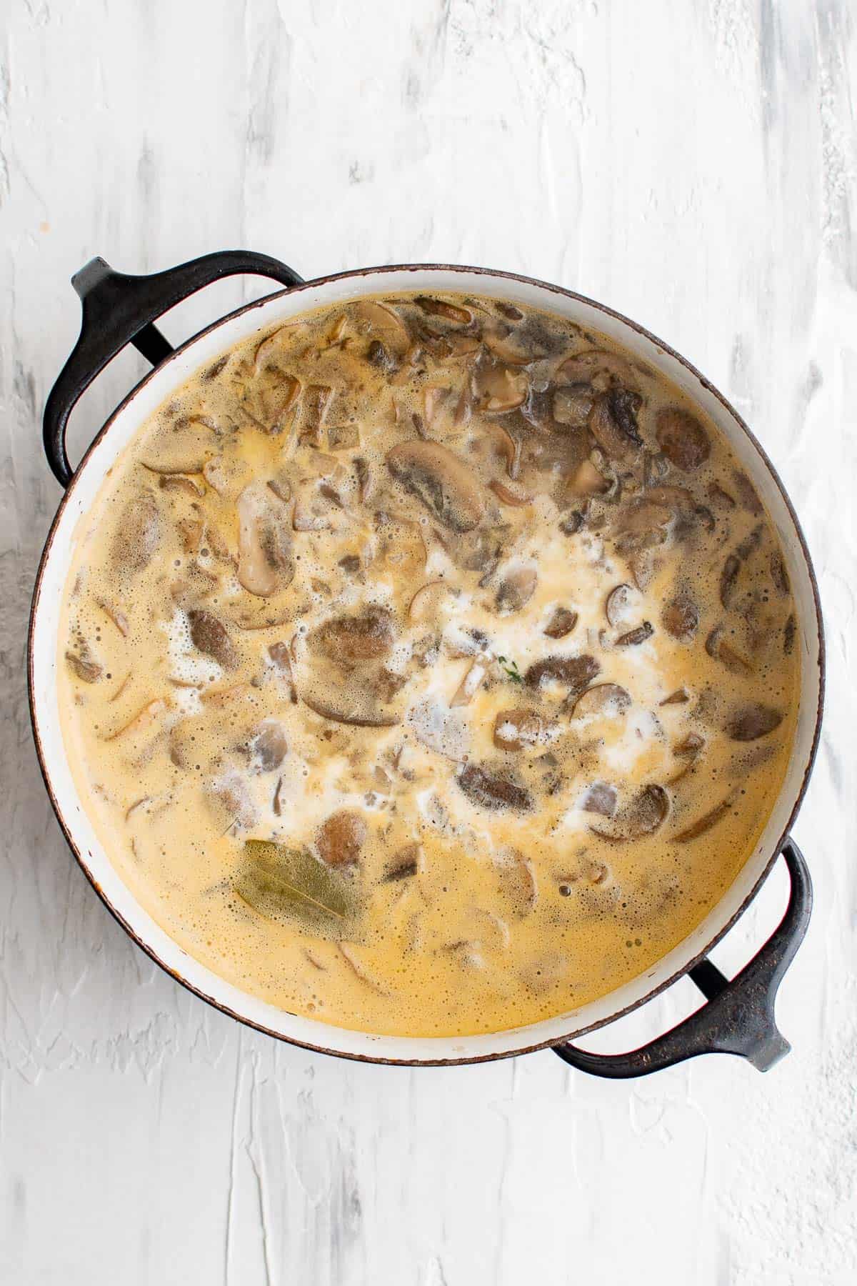 dutch oven with chicken stock, cream, sautéed mushrooms, garlic, onion, thyme, bay leaves, salt, and pepper for creamy mushroom soup