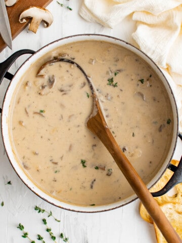 a pot of cream of mushrooms soup, with a wooden ladle, served with bread