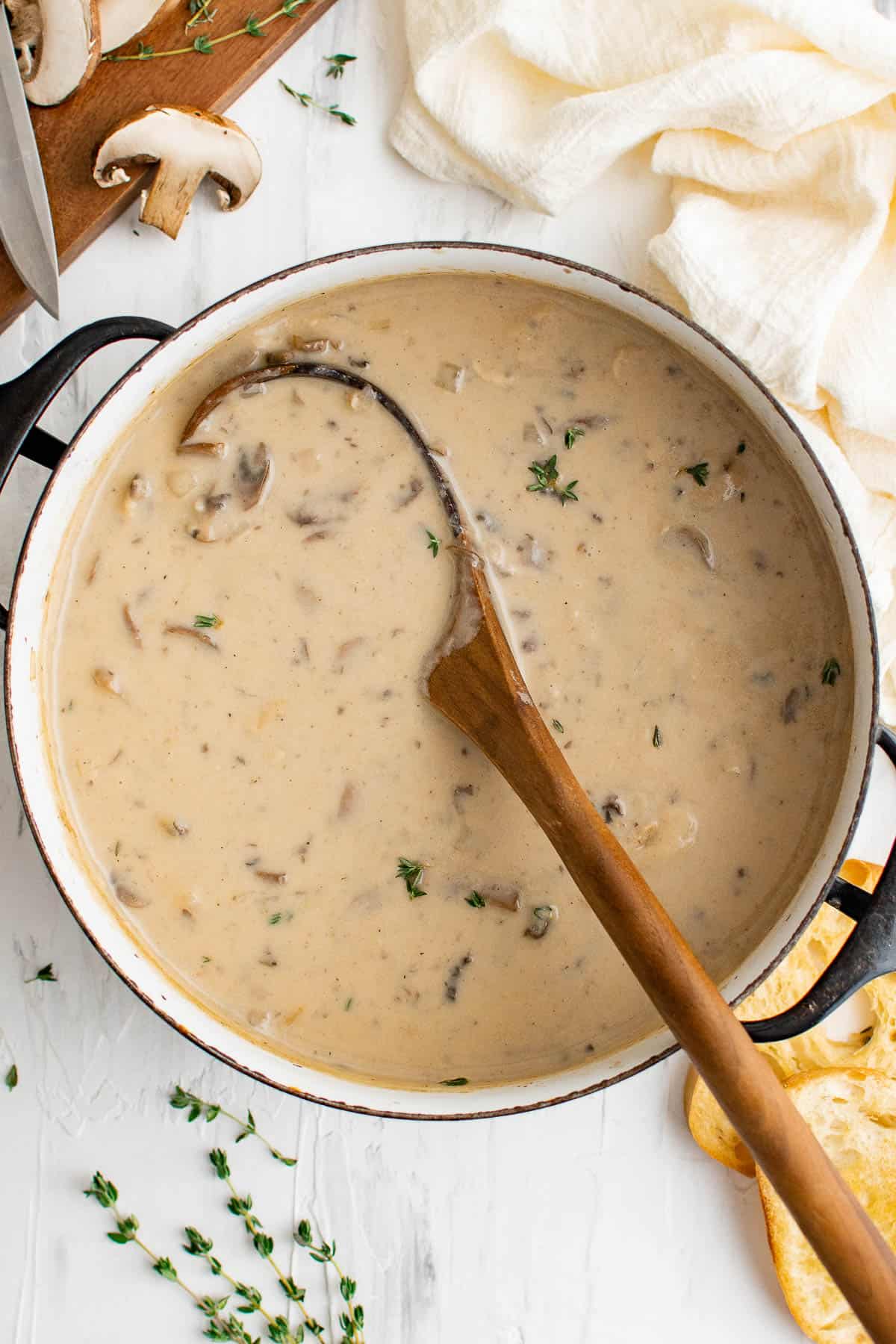 a pot of cream of mushrooms soup, with a wooden ladle, served with bread