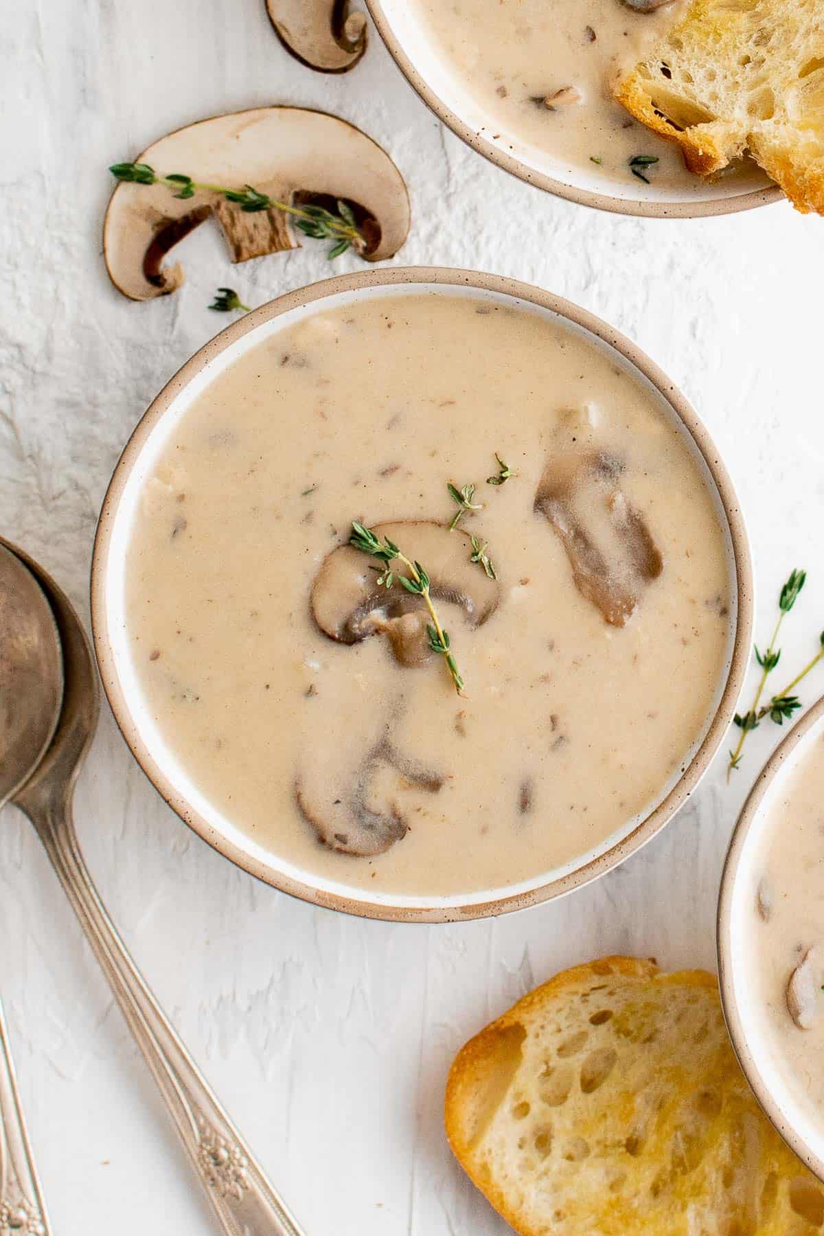 a bowl of mushrooms soup, garnished with fresh thyme and served with bread
