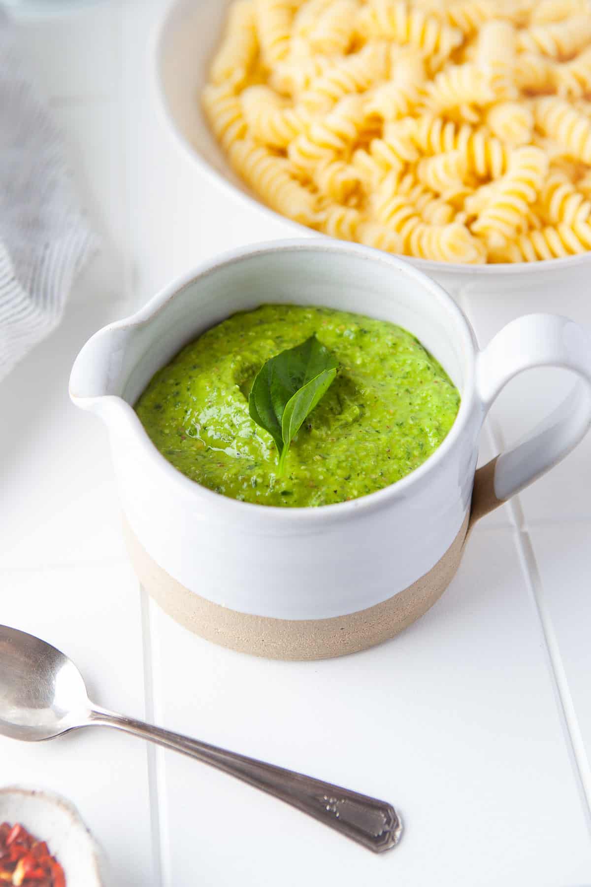 a white serving dish full of homemade pesto, with a bowl of fresh pasta in the background