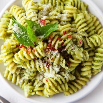 a white bowl full of homemade pesto pasta, topped with parmesan and basil