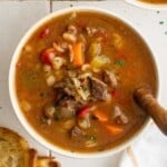 a big bowl of vegetable beef barley soup, with a wooden spoon