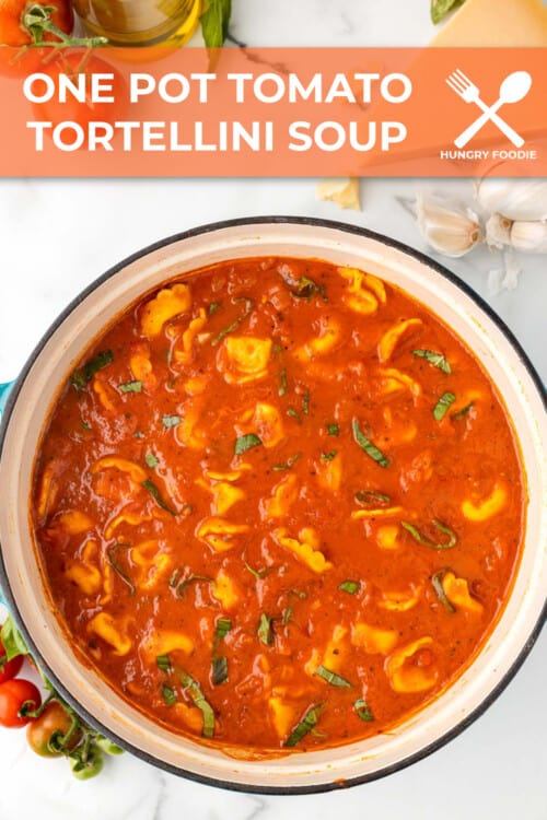 a dutch oven full of creamy tomato soup with cheese stuffed tortellini and garnished with fresh basil