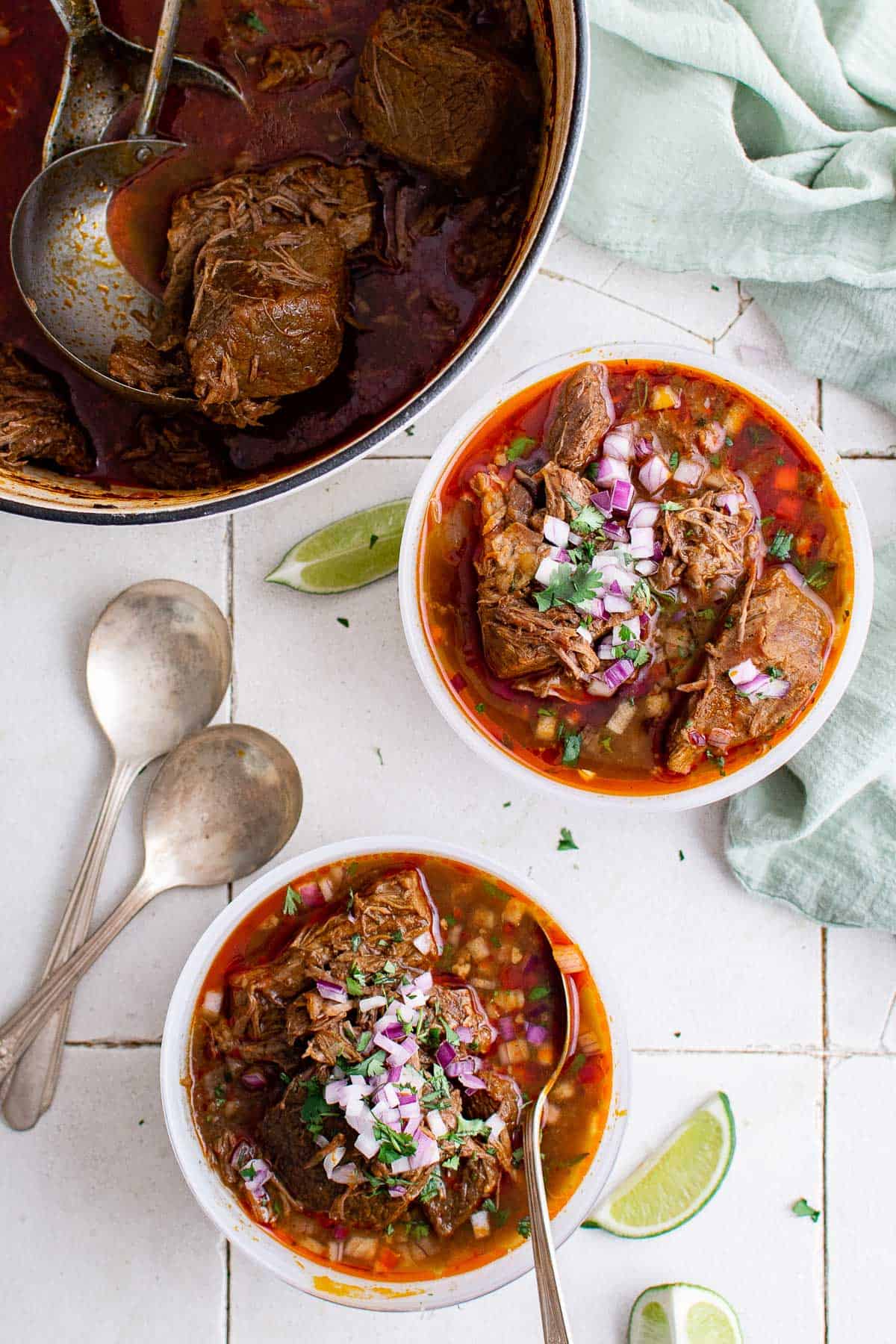 2 bowls beef birria Mexican stew, garnishes with red onion, cilantro and lime