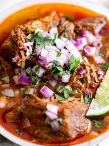 a bowl of beef birria Mexican stew, garnishes with red onion, cilantro and lime