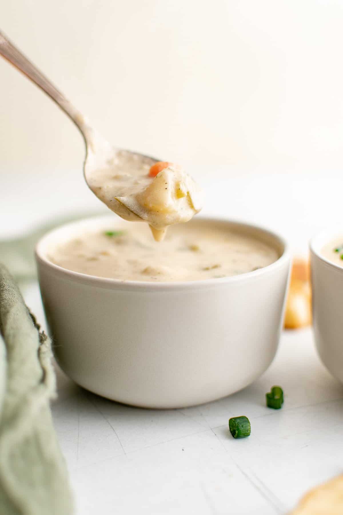 a white bowl full of creamy soup, garnished with green onions and served with bread