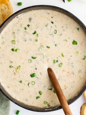 a cast iron pot full of dill pickle soup, garnished with green onions and served with bread