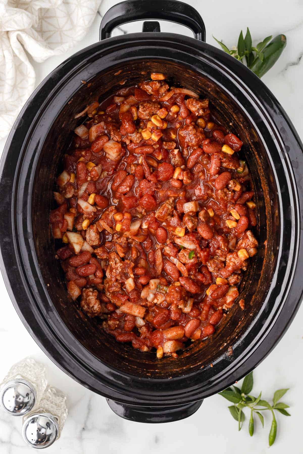 A slow cooker loaded up with ground turkey, beans, corn, onion, garlic, jalapeños, tomatoes and warm spices to make homemade chili