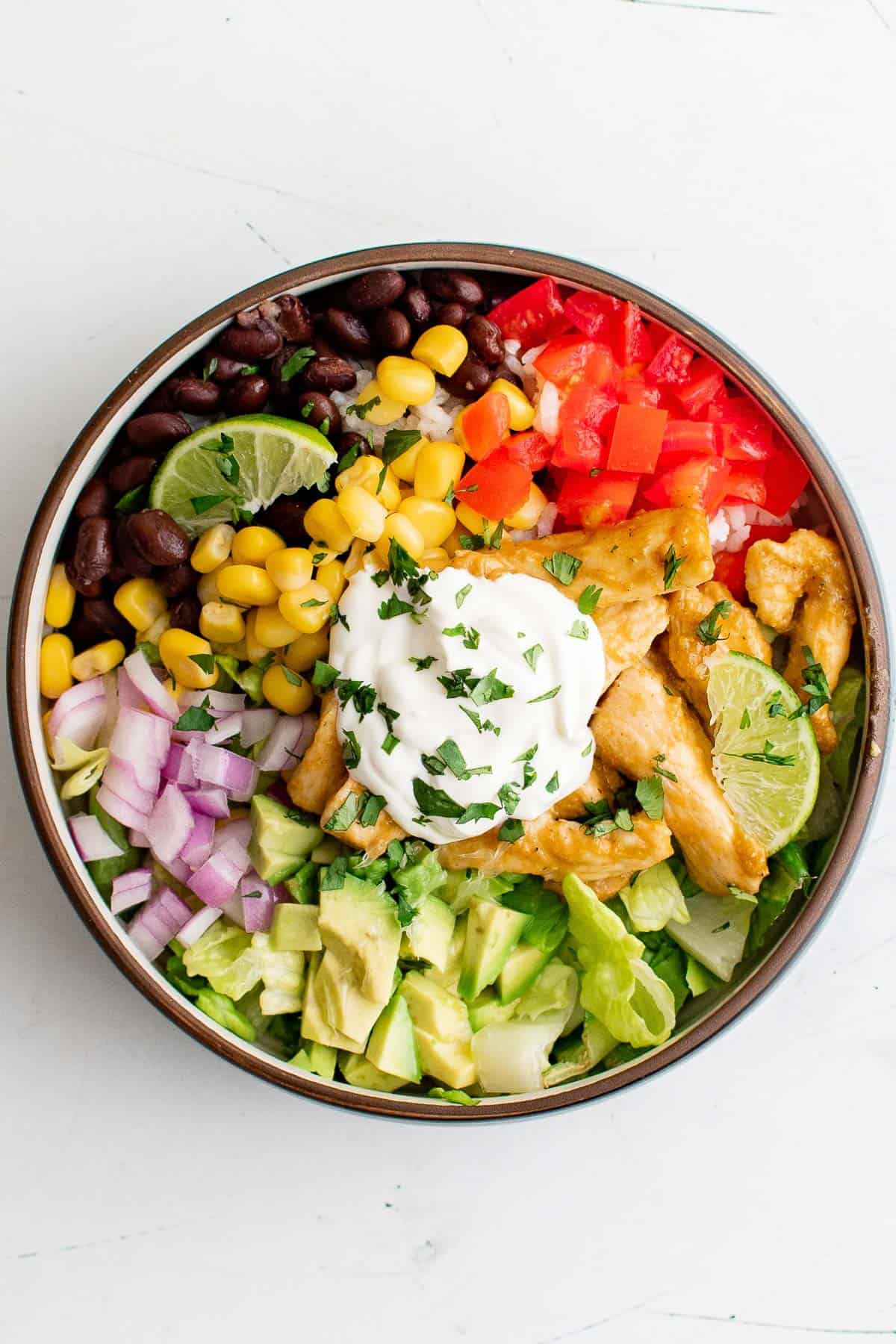 a chicken burrito bowl, filled with chicken, onion, corn, beans, rice, avocado, and sour cream