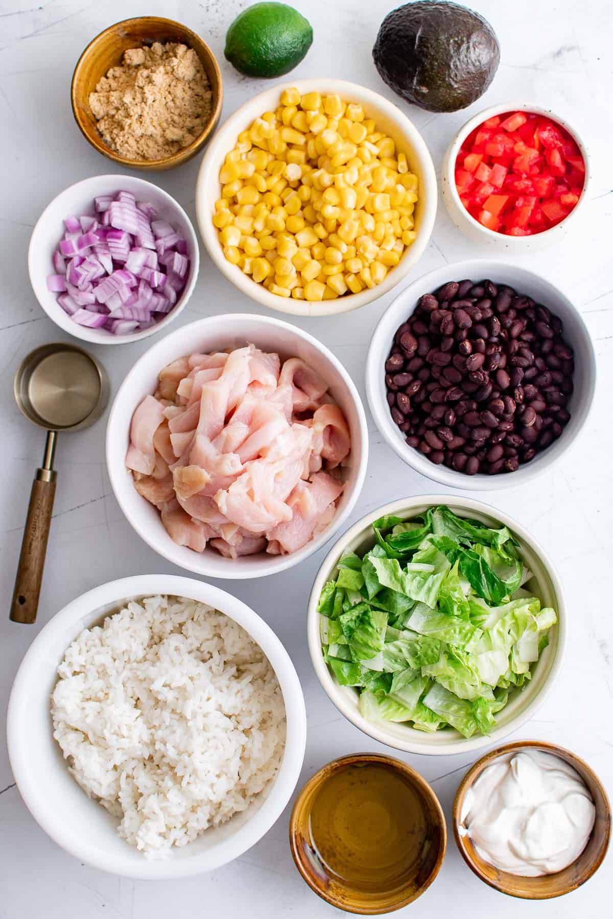 Ingredients to make burrito bowls -  chicken, onion, corn, beans, rice, avocado, lettuce and sour cream
