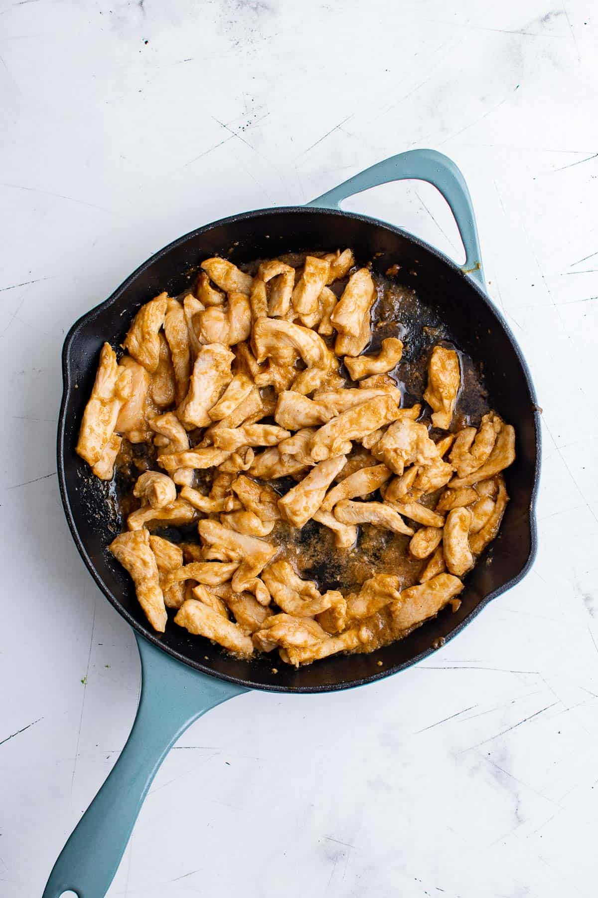 sliced chicken breast being cooked in a cast iron skillet in olive oil, water, and fajita seasonings