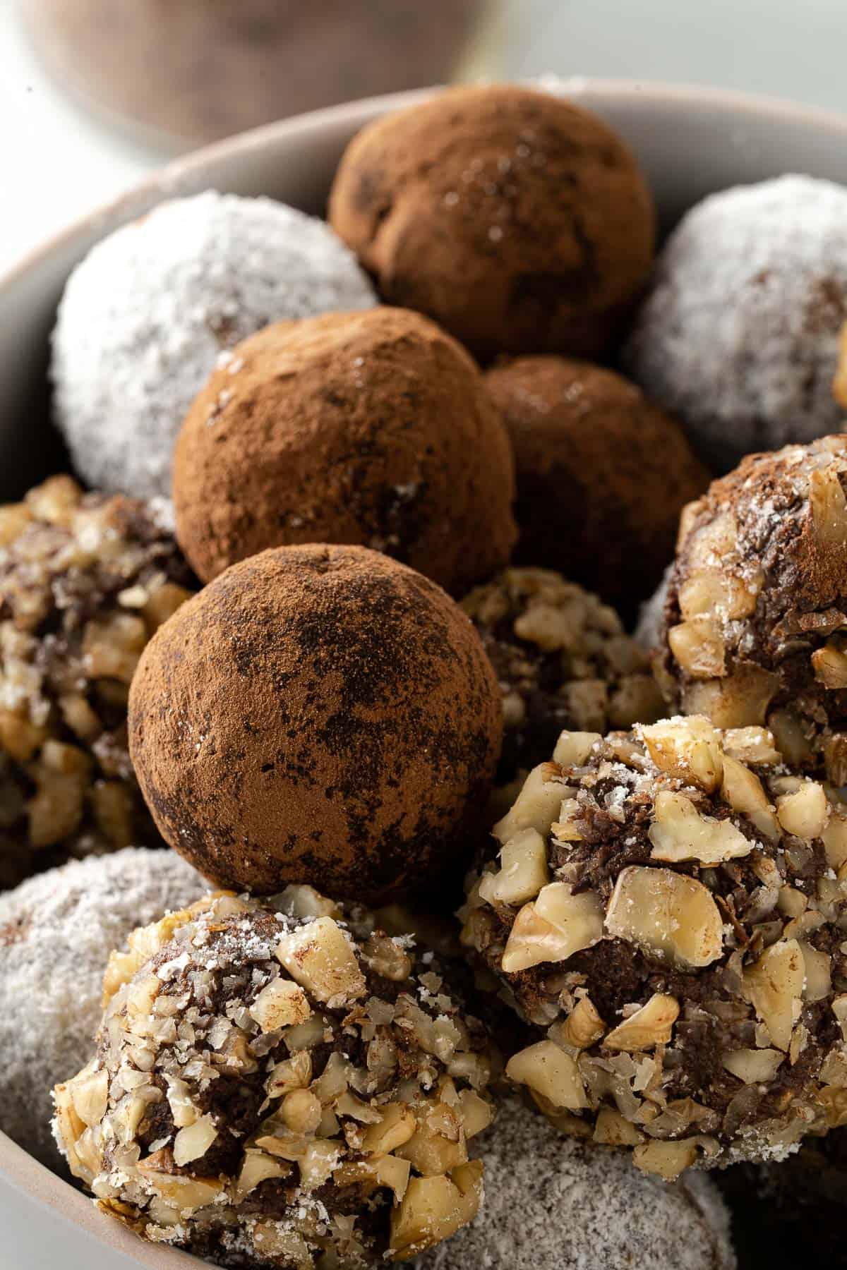 a bowl of assorted chocolate truffles, covered with cocoa powder, coconut, and walnuts
