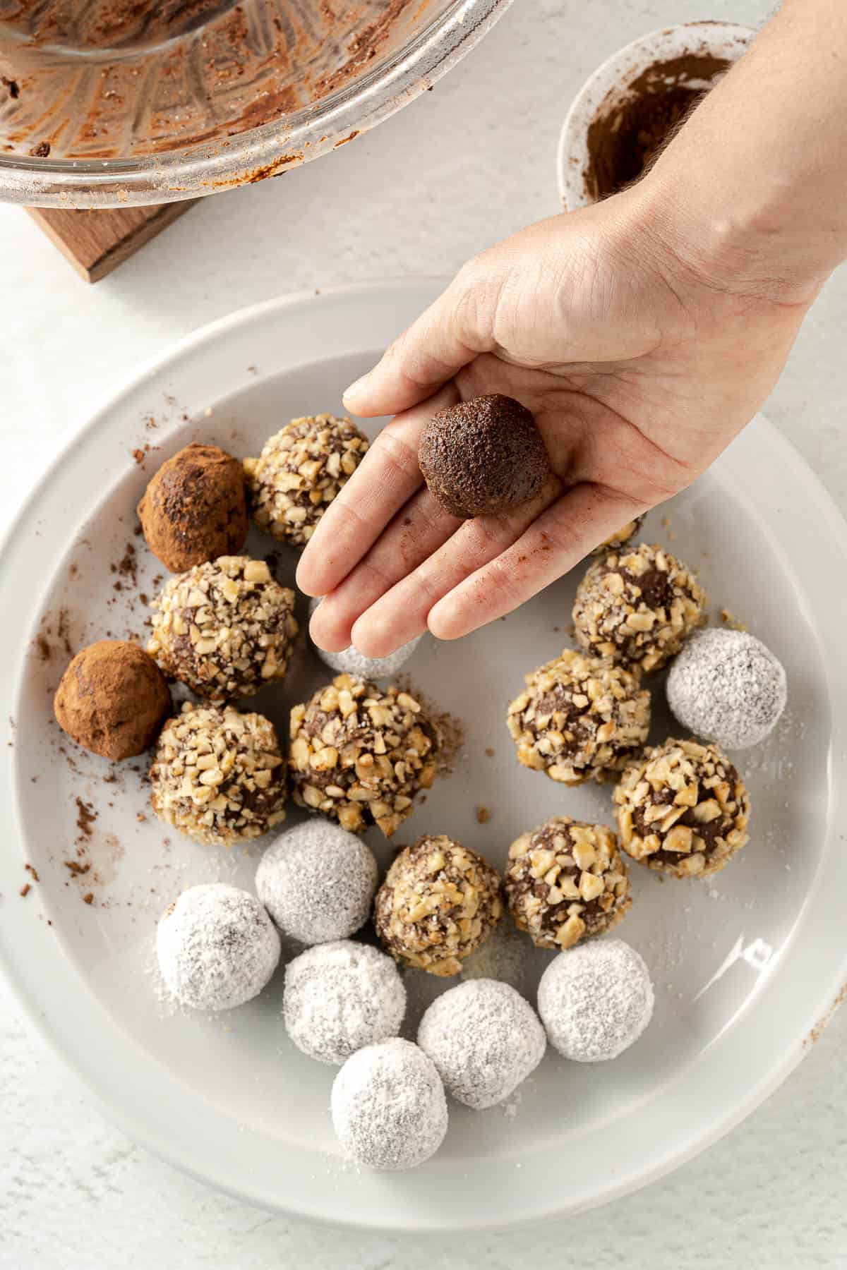 a plate of chocolate truffles, rolled up and coated in coconut, cocoa powder and crushed walnuts