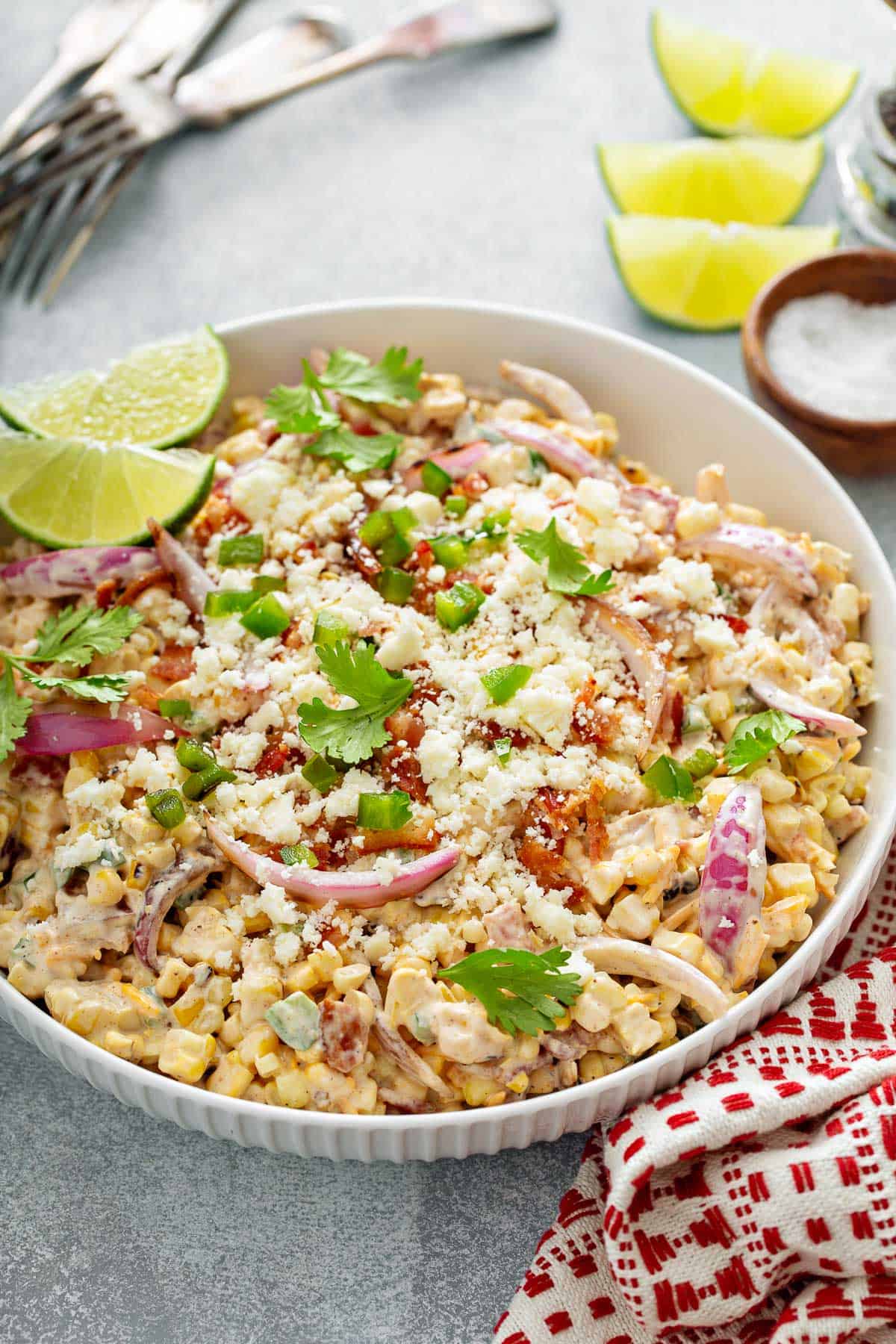 a white bowl full of corn salad with corn, red onion, bacon, cheddar, jalapeños, cilantro and bacon