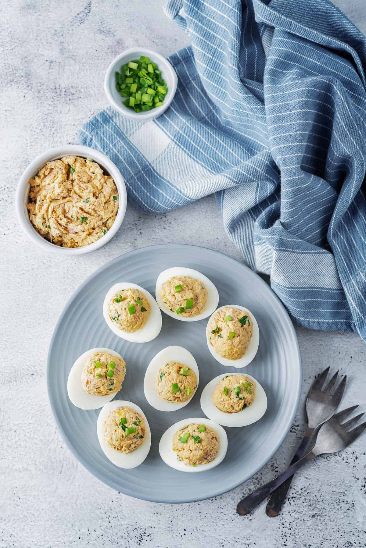 a blue plate topped with deviled eggs, with a blue towel and chopped green onions in the background