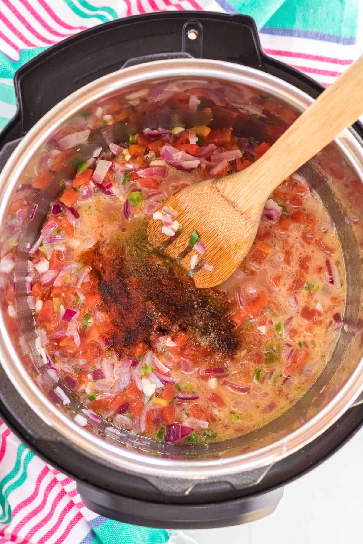 an instant pot with red onion garlic, jalapeños, tomatoes, and seasonings.