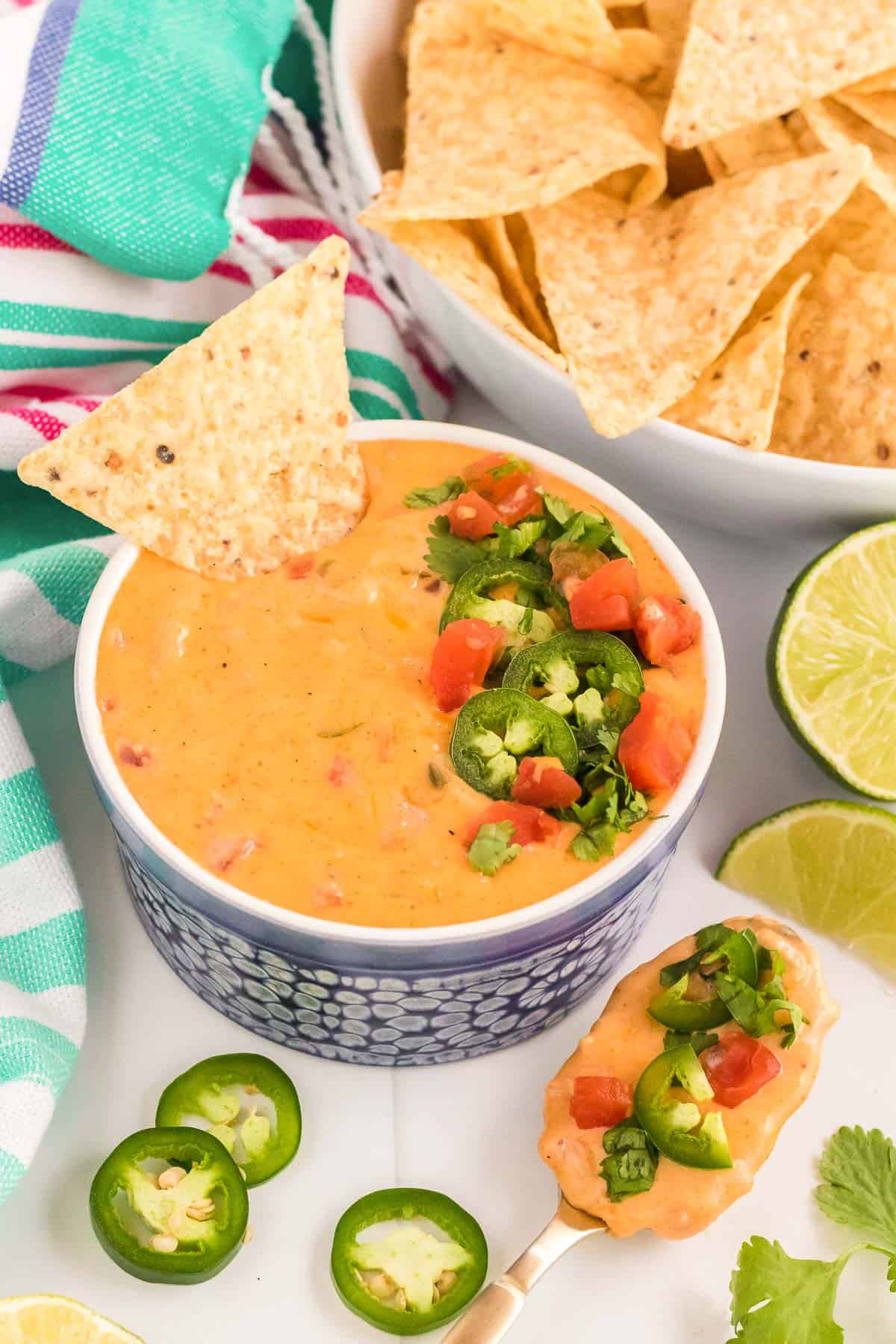 a bowl of queso dip, surrounded by limes, cilantro, jalapeños and chips.