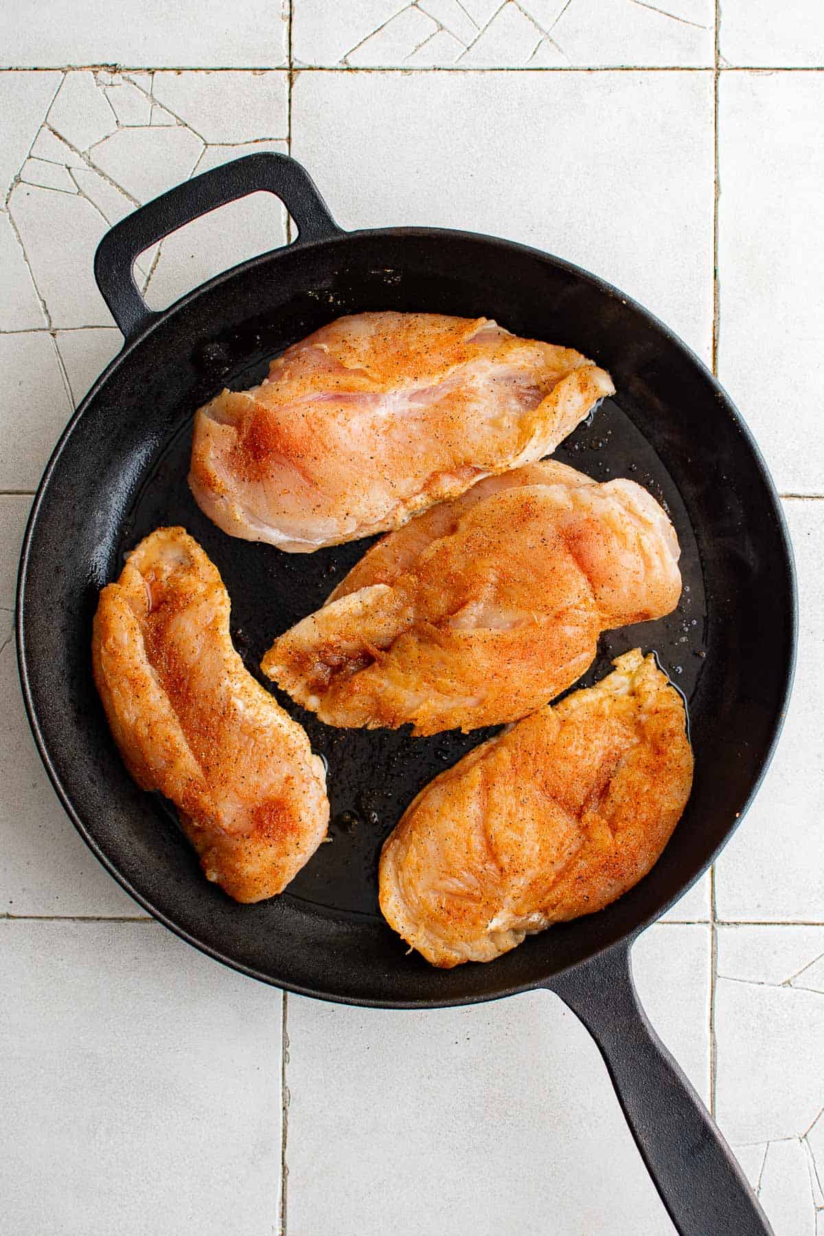 seasoned, raw chicken breasts in a cast iron skillet.