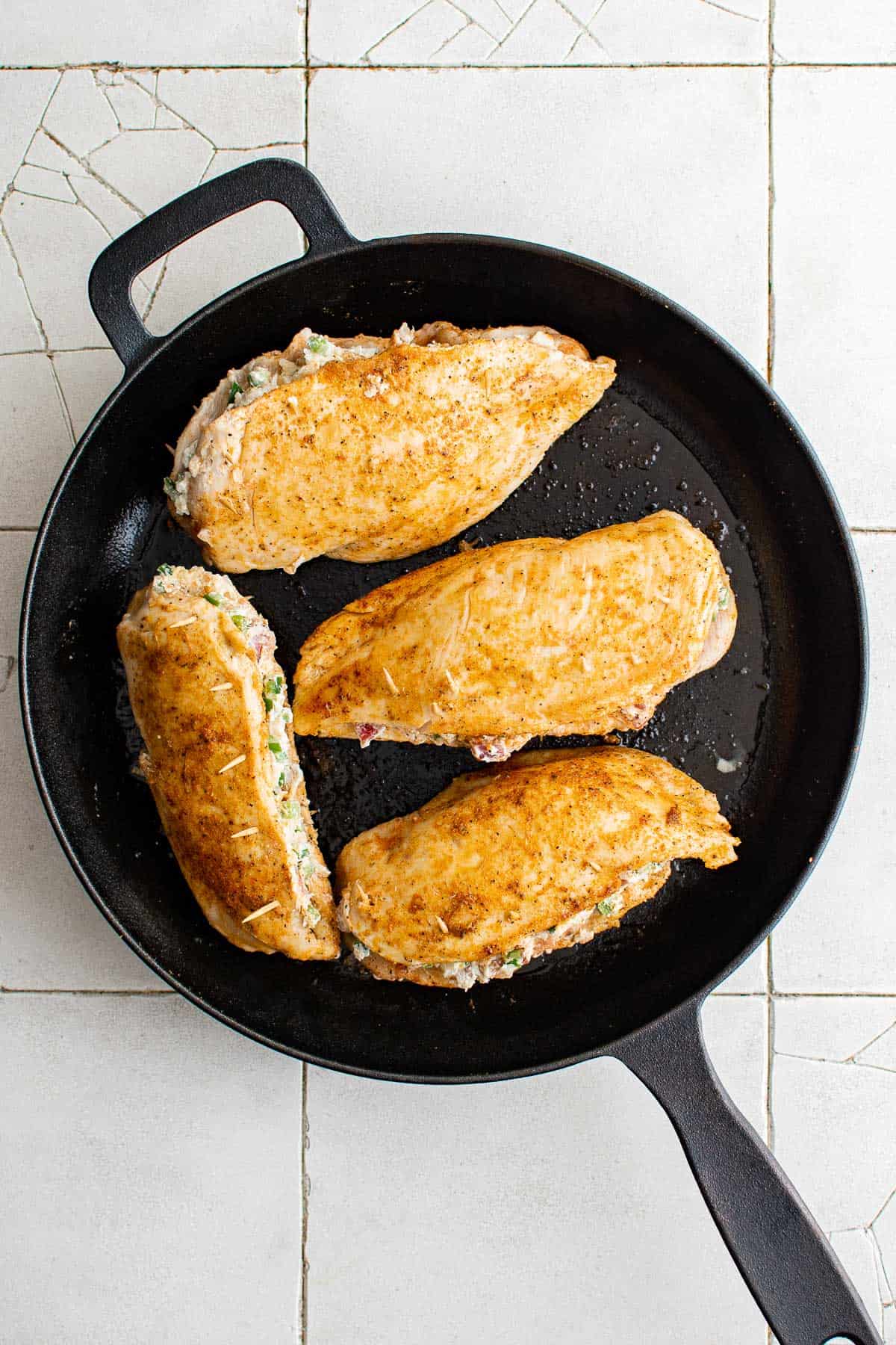 Seasoned and stuffed chickens being pan-seared in a cast iron skillet.