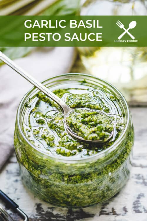 a glass jar of fresh made pesto, with a serving spoon balancing on top.