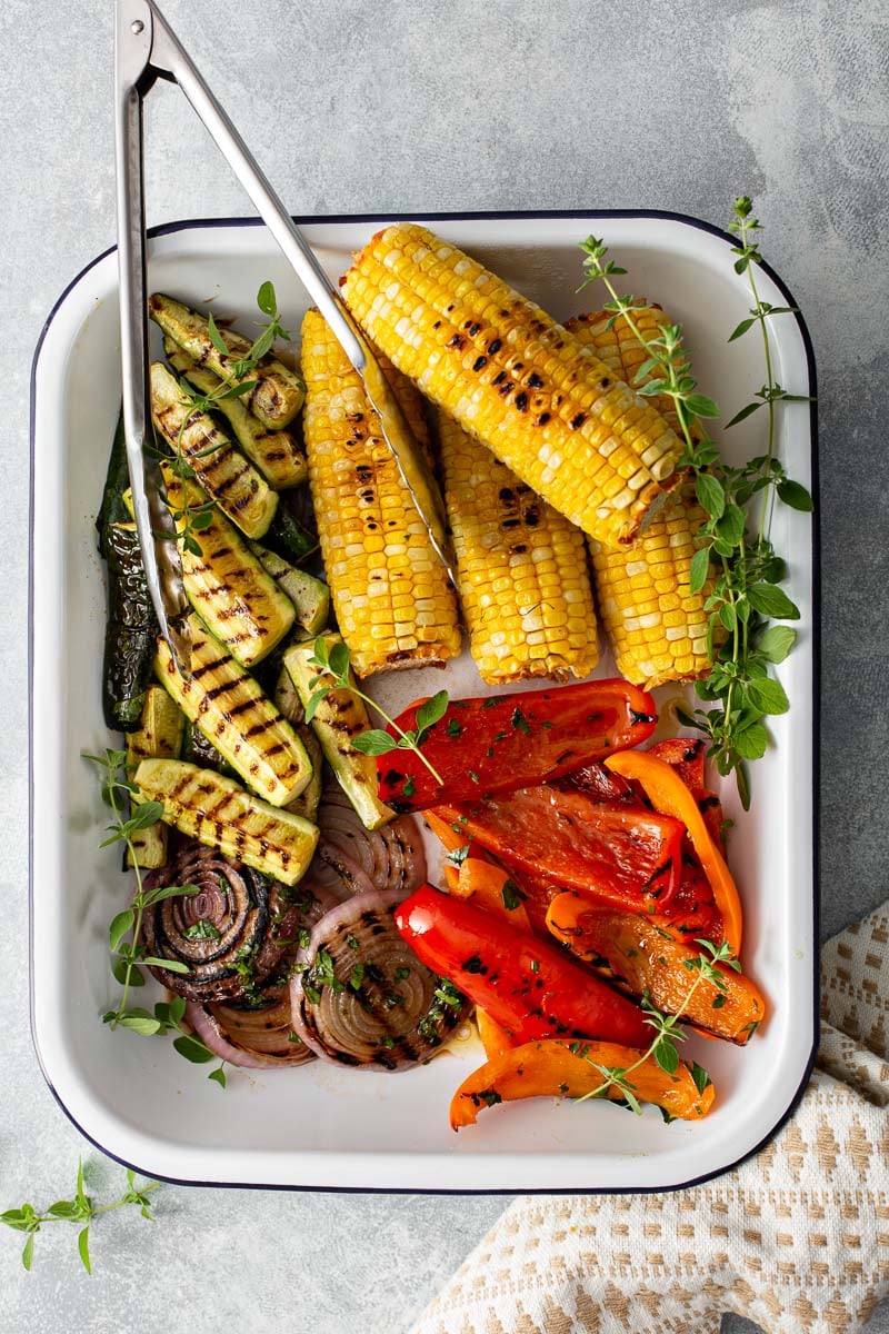 a rimmed baking sheet with grilled corn, red onion, bell peppers, and zucchini.