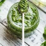 a glass jar of fresh made pesto, with a serving spoon balancing on top.