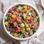 a quinoa salad with tomatoes, cucumber, red onion, mandarins, bell peppers and parsley.