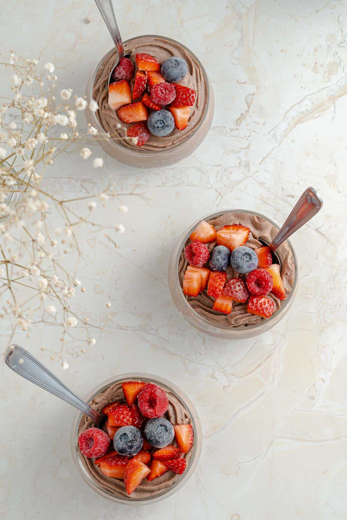 3 glass jars full of chocolate cheesecake mousse, topped with frozen mixed berries.