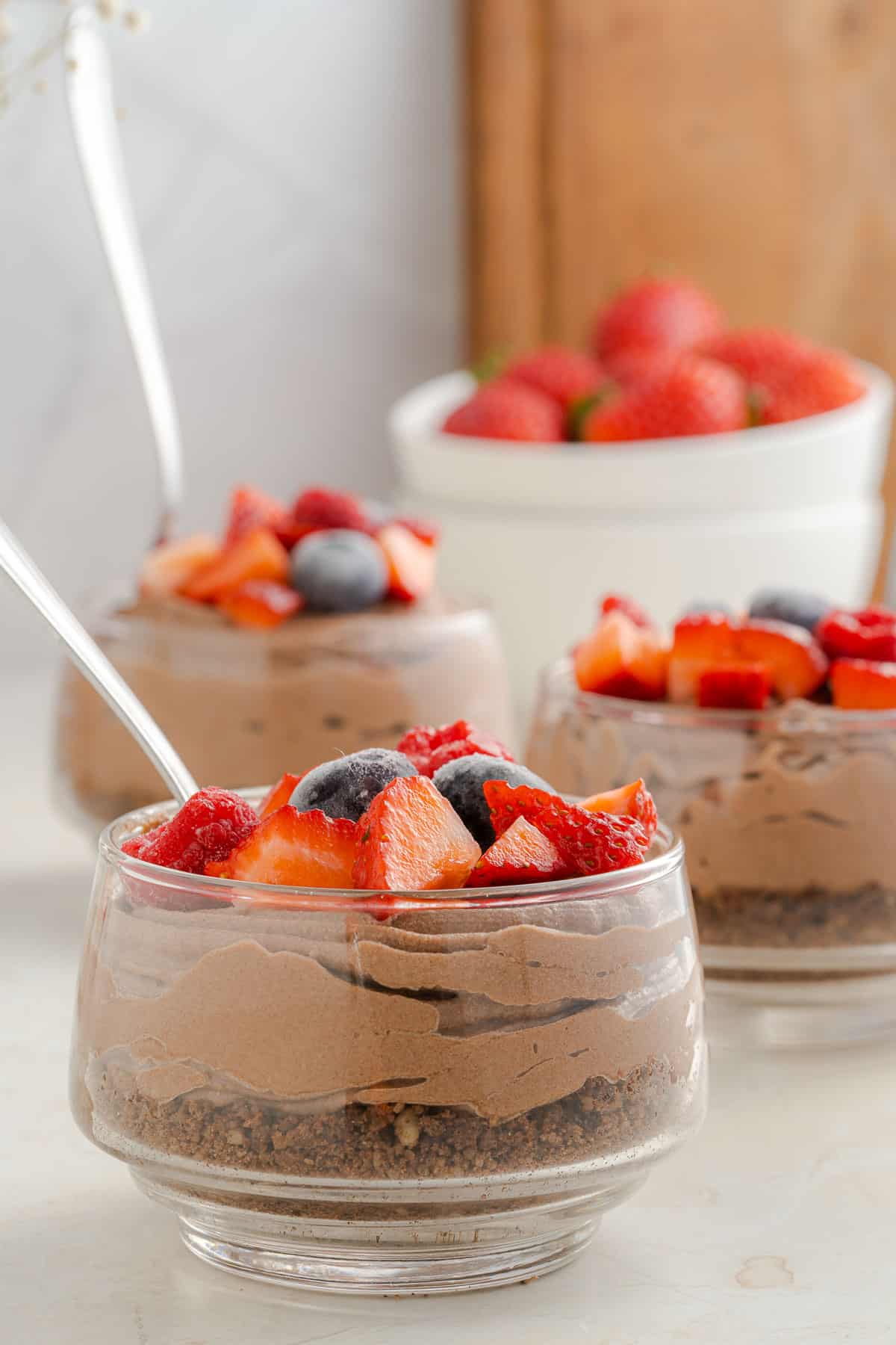 3 glass jars full of chocolate cheesecake mousse, topped with frozen mixed berries.