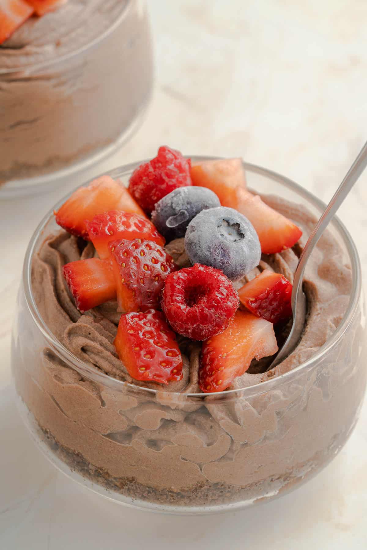 a glass jar full of chocolate cheesecake mousse, topped with frozen mixed berries.