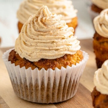 A wooden cutting board with low carb pumpkin cupcakes, topped with cream cheese frosting and sprinkled with cinnamon.